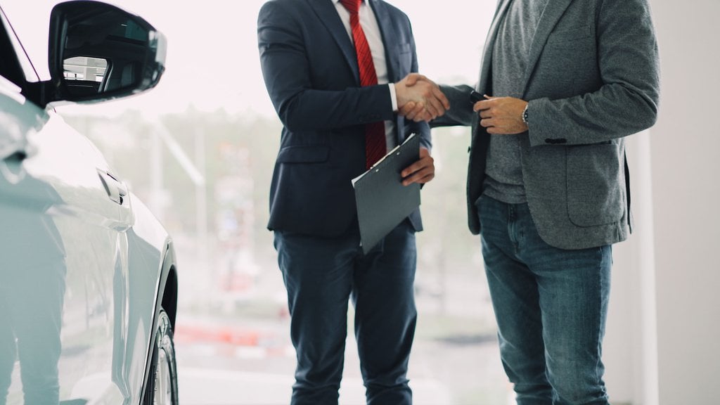 Un conseiller automobile serre la main d'un client à côté d'un véhicule dans un showroom.