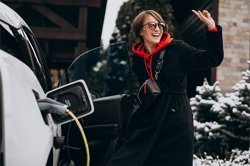 Une femme qui charge son véhicule électrique alors qu'il neige