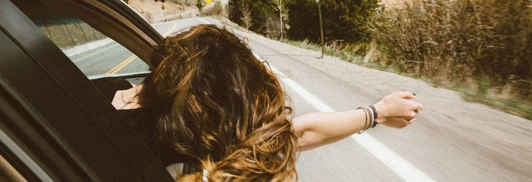 woman riding on vehicle putting her head and right arm outside the window while travelling the road